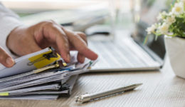 Businessman hands holding pen for working in Stacks of paper files searching information business report papers and piles of unfinished documents achieves on laptop computer desk in modern office Businessman hands holding pen for working in Stacks of paper files searching information business report papers and piles of unfinished documents achieves on laptop computer desk in modern office